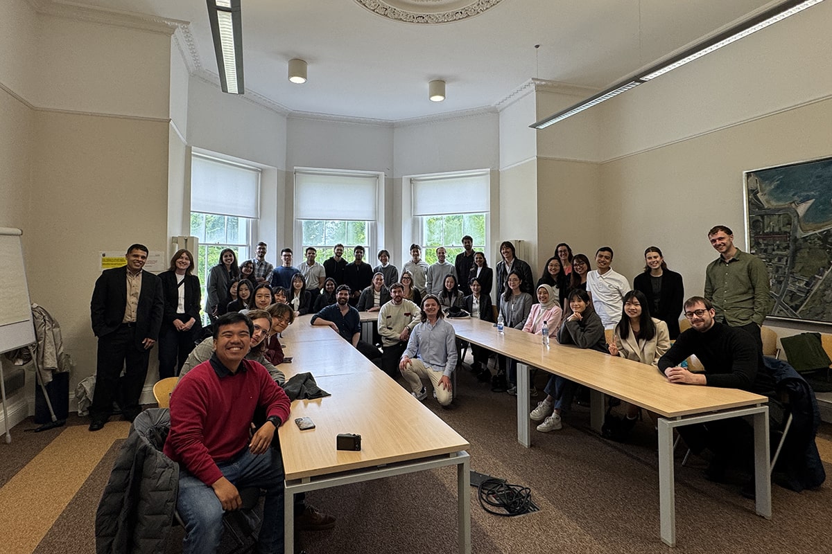 About 30 students gathered at a table in a room, participating in a collaborative meeting or discussion.