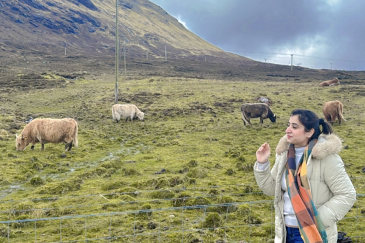 Pranshi standing in front of a field of cattle with Scottish hills in the background