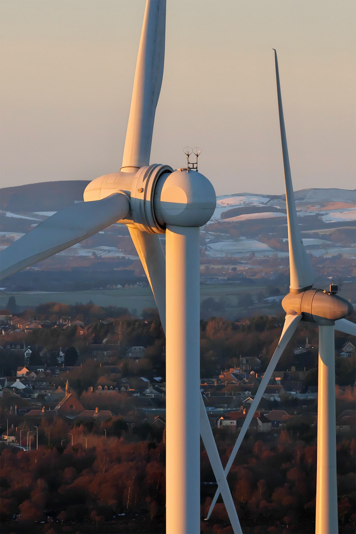 Wind turbines rise above a Scottish town, set against a picturesque landscape of hills.