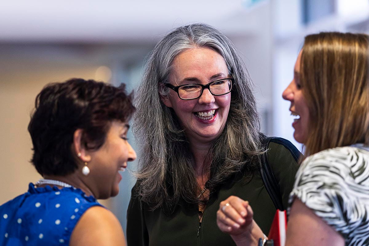 Three smartly dressed people in conversation smiling