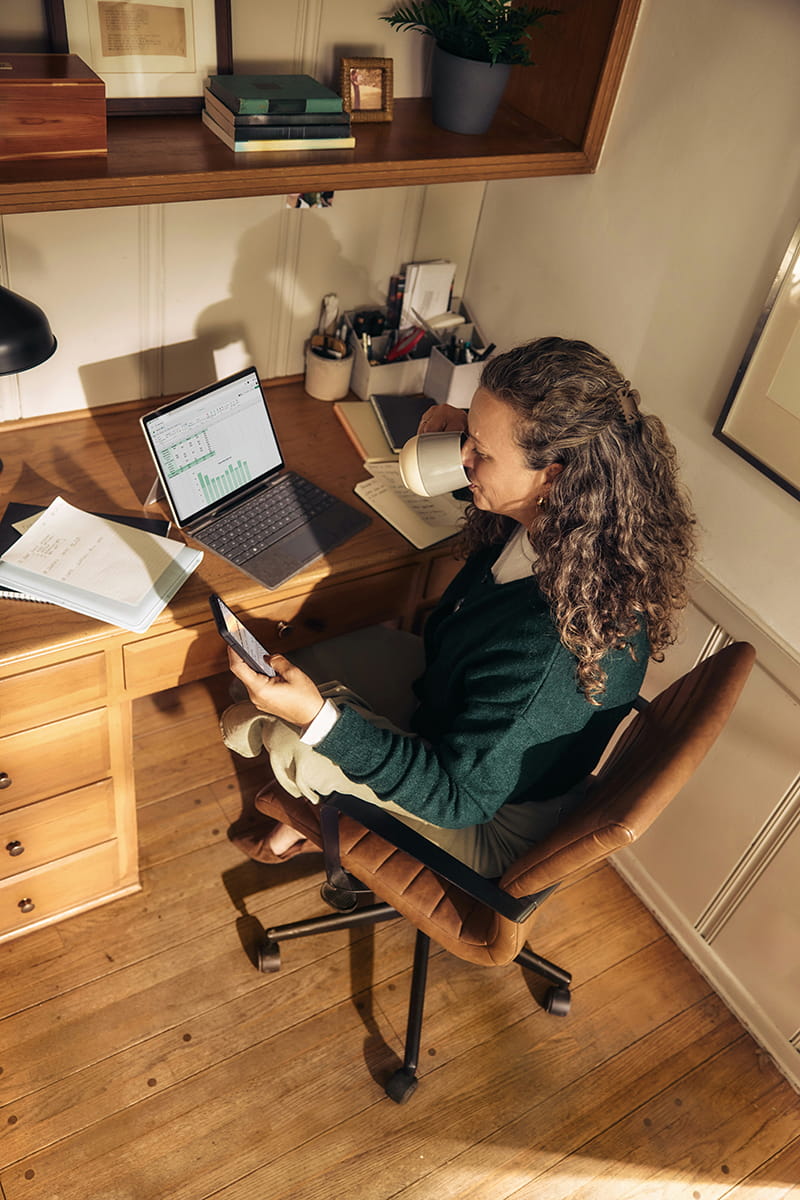 Person using mobile phone whilst sitting at desk in front of laptop