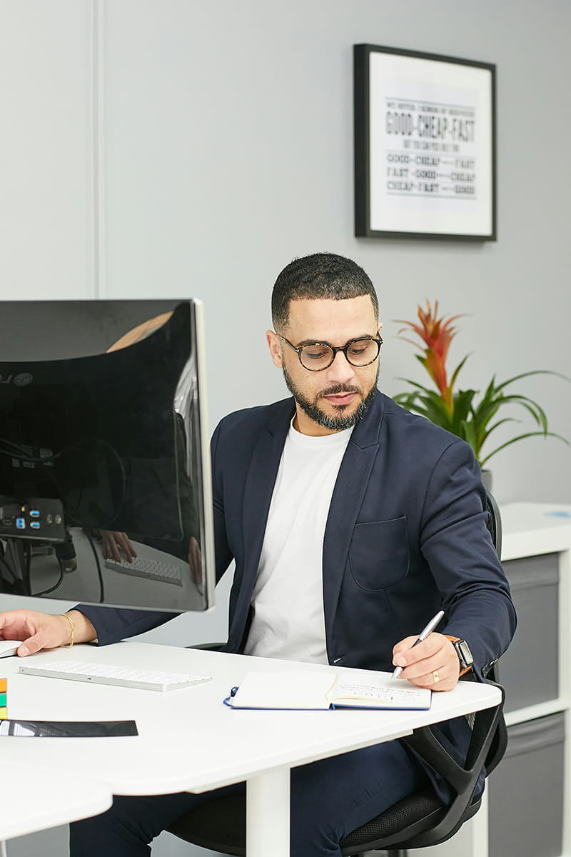 Person taking notes whilst sitting at a desk in front of a computer screen