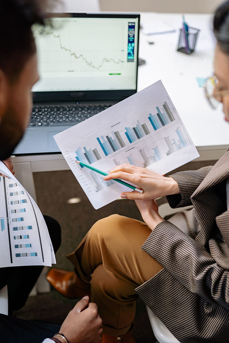 Two people sitting at a desk studying financial data  paperwork with a laptop in front of them
