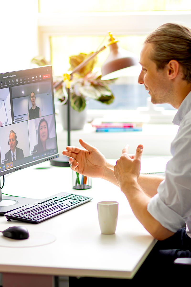 An individual seated at a desk engaged in an online meeting displayed on their computer screen.