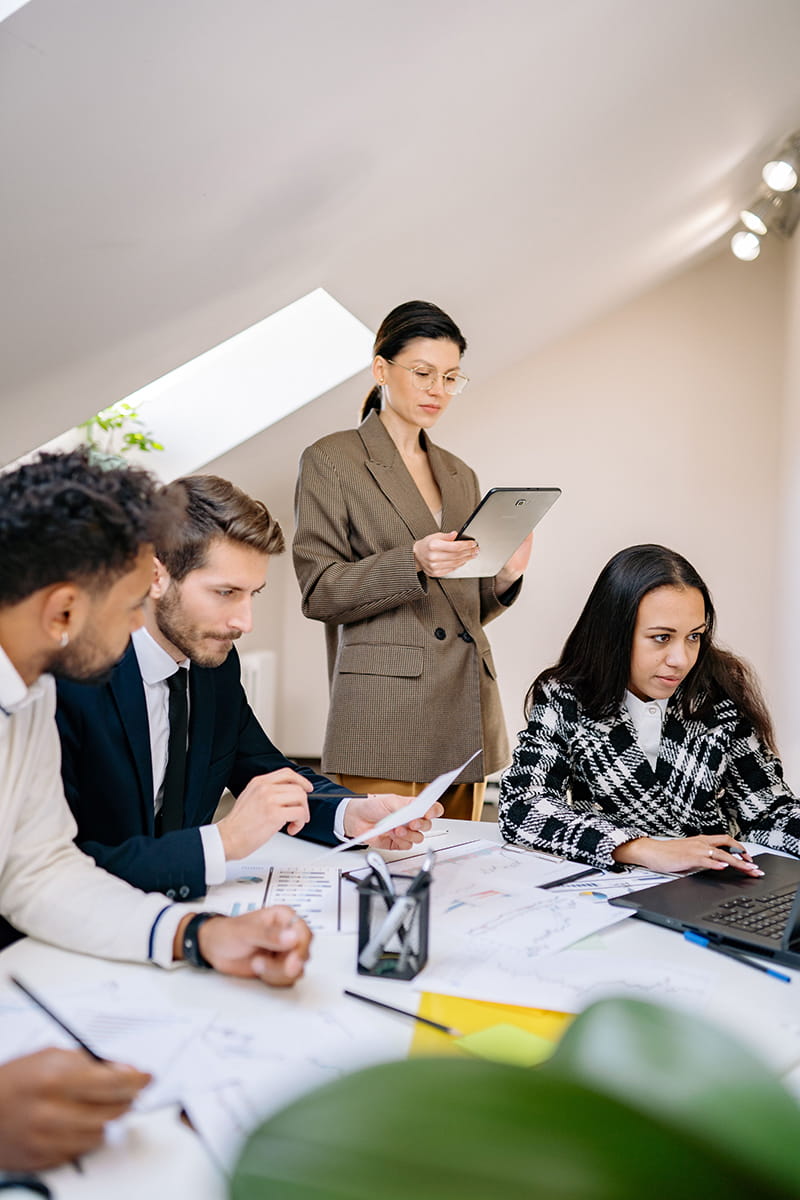 Group of 4 business people looking at paperwork together around a desk 