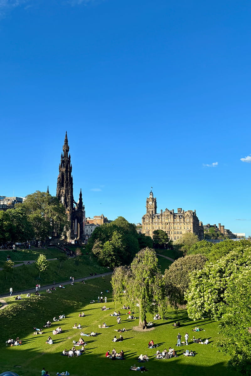 View of Princes Street Gardens in Edinburgh featuring the Scott Monument, set against a clear blue sky.
