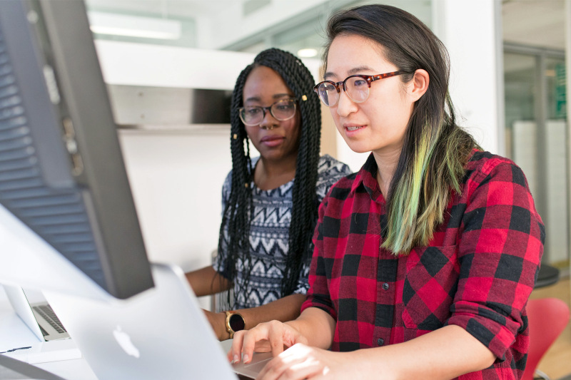 Two women sitting at a desk looking at a laptop