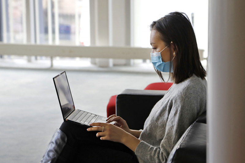 student with a mask sitting and typing on a laptop