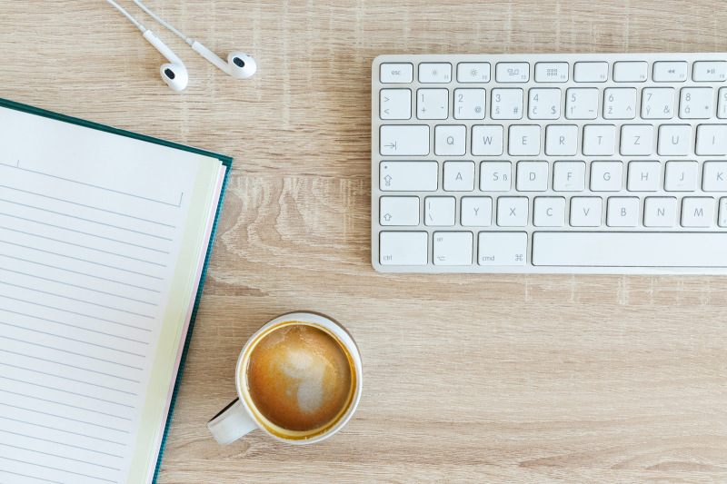 A desk with a coffee, notebook, earbuds and keyboard