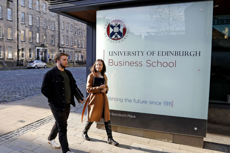 Business School building front with two students walking past