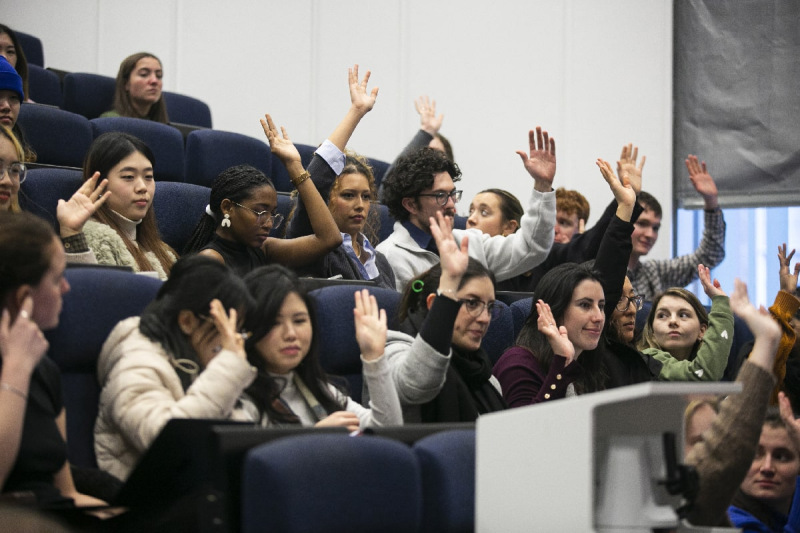 Students with their hands up asking questions in lecture theatre