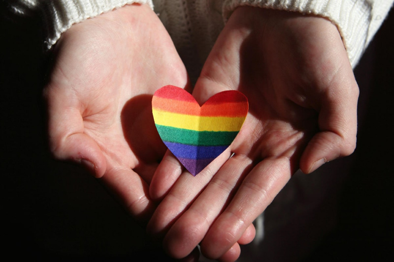 Person's hands holding paper rainbow coloured heart