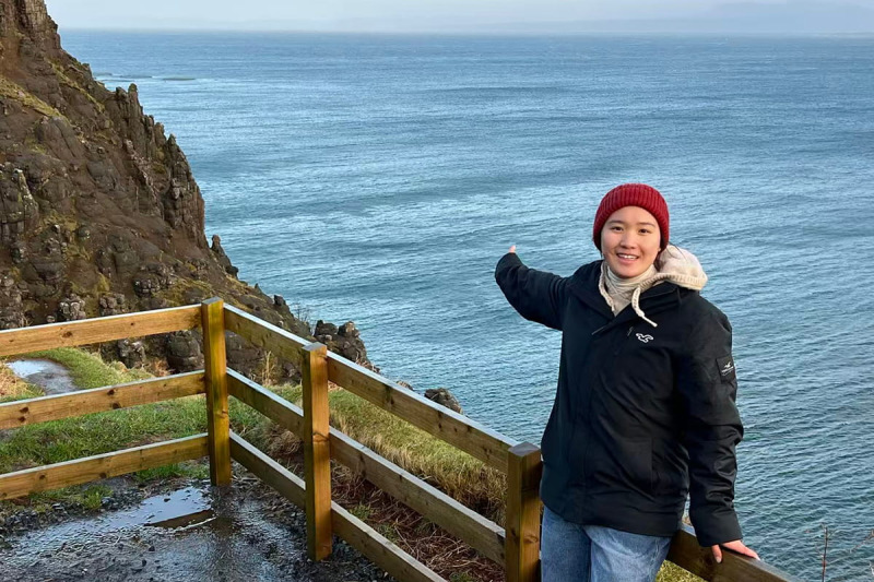 Student dressed for a cold Scottish day pointing at the sea