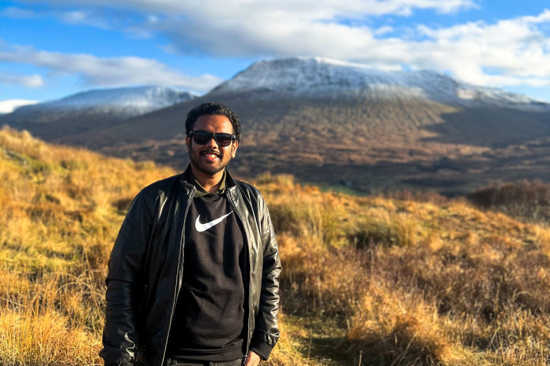 Sidhanth standing smiling in front of mountains in the Scottish Highlands