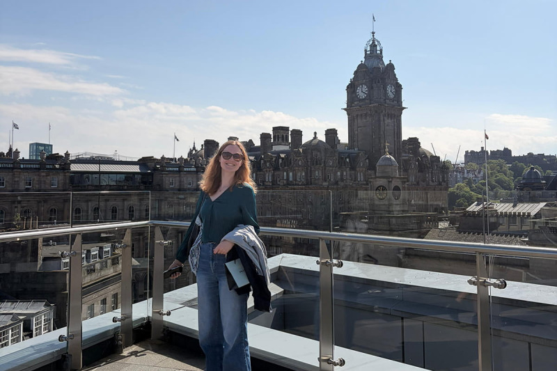 MSc student standing on a rooftop balcony with Edinburgh buildings in the background.