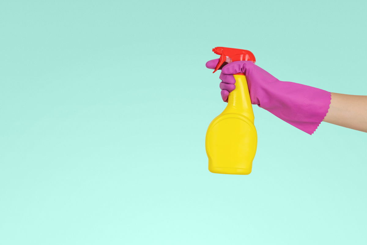 Person holding cleaning spray wearing marigolds