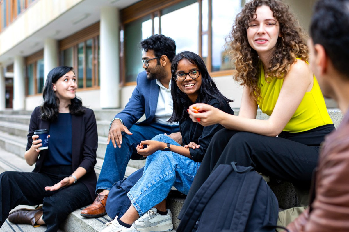 Four sudents sitting on the steps outside the  University of Edinburgh Business School