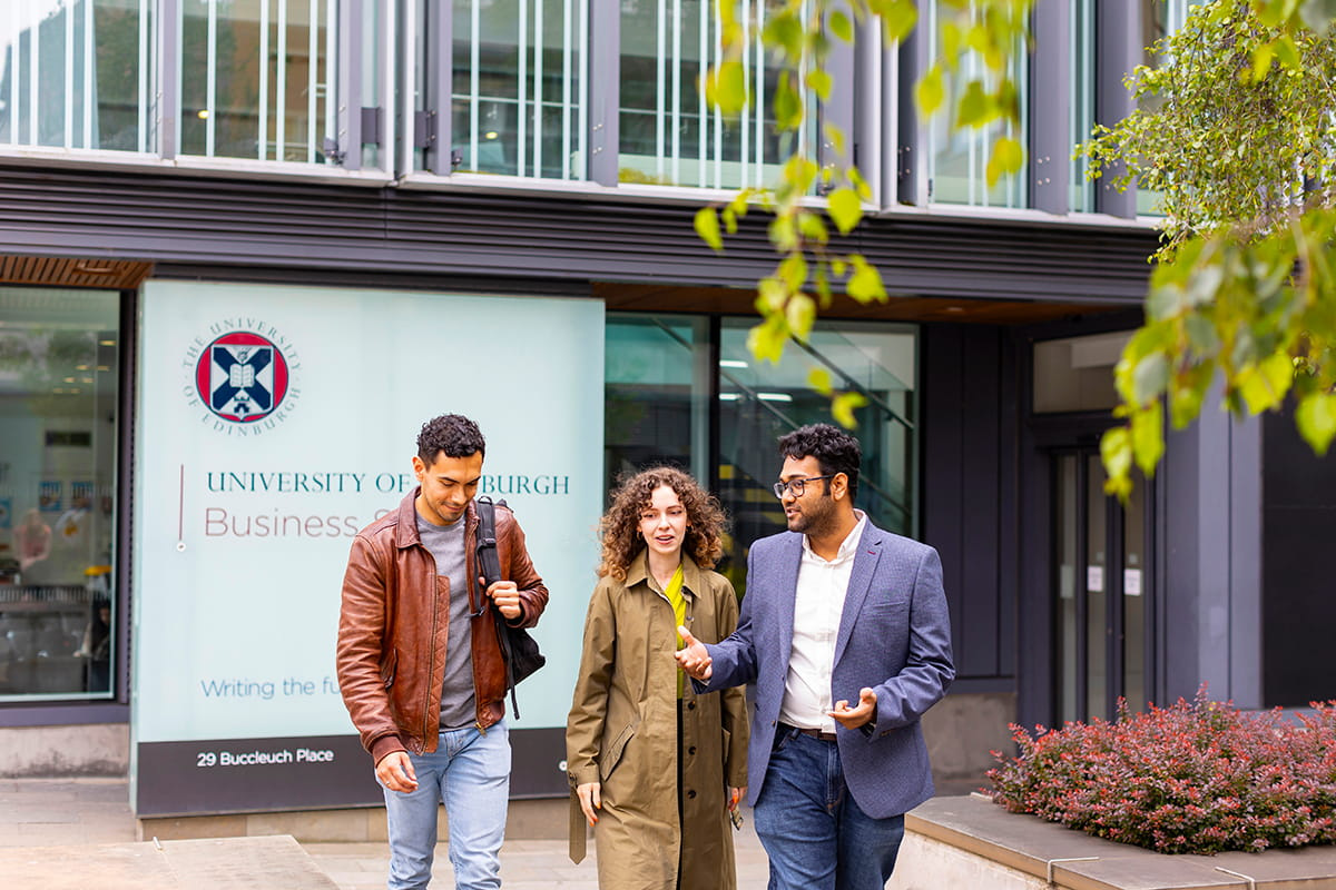 Three students walking in conversation outside the entrance to the University of Edinburgh Business School