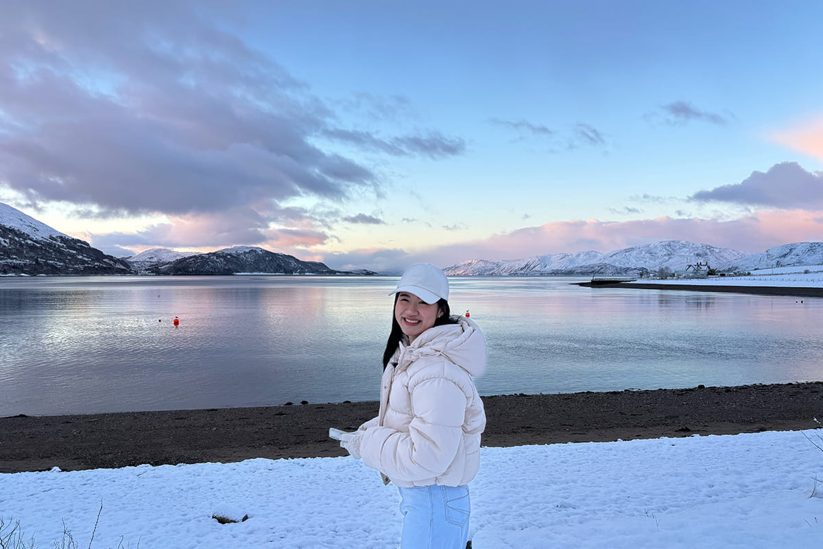 Student standing and smiling in front of a loch in the Scottish Highlands during winter, with snow-covered hills in the background.