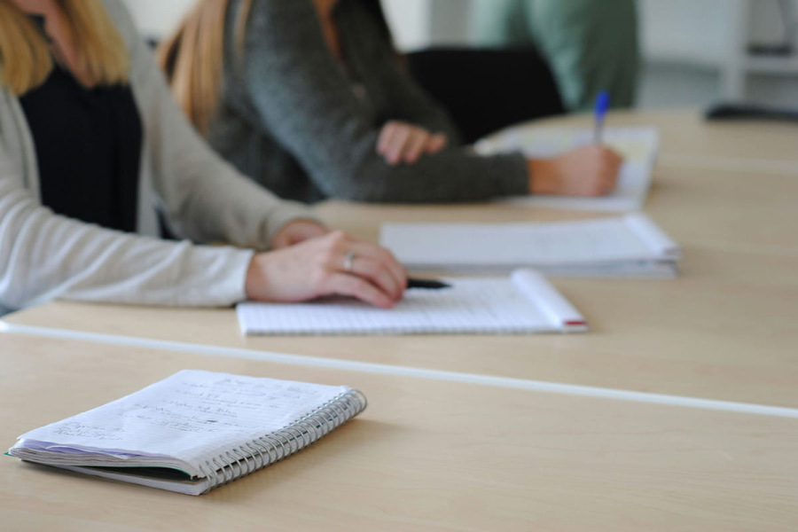 Hands resting on work notepad, whilst colleague is sitting at desk. Credit sarah b (unsplash)